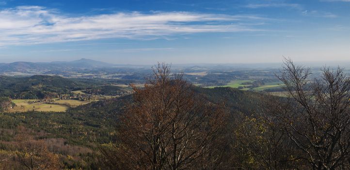 Luzicke hory wide panorama, panoramic view from Hochwald Hvozd one of the most attractive view-points of the Lusatian Mountains with autumn colored deciduous and coniferous tree forest and green hills, golden hour light.