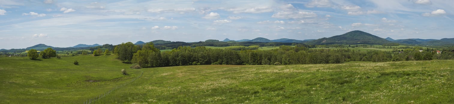 idyllic spring panoramic landscape in lucitian mountains, with lush green grass meadow, fresh deciduous and spruce tree forest, hills, blue sky white clouds background, horizontal, copy space.