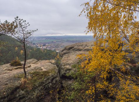 Panoramic view from sandstone pillars view-point at nature reserve Cesky Raj with autumn colored deciduous and coniferous tree forest and green hills, moody blue sky.