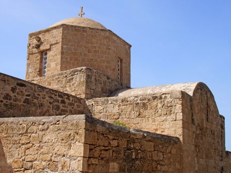 close up of the ancient church of Ayia Kyriaki Chrysopolitissa in paphos cyprus showing the basilica shaped structure and tower against a blue sunlit sky