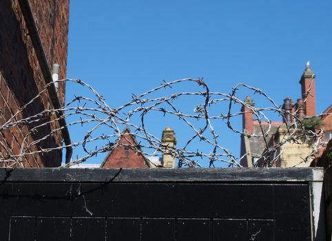 barbed wire on top of a wooden fence surrounded by urban buildings against a blue sky