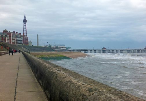 a view of blackpool promenade in winter with stormy sea tower and central pier with unidentifiable people walking along the seafront