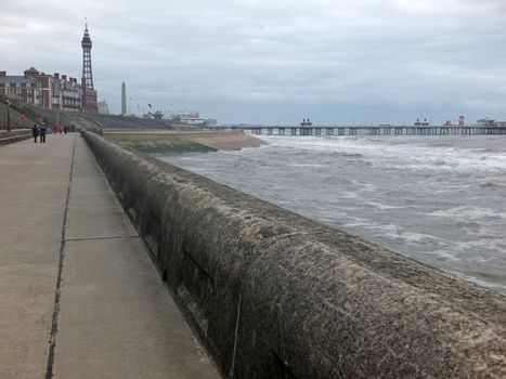 a view of blackpool promenade in winter with stormy sea tower and central pier with unidentifiable people walking along the seafront