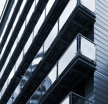 blue toned corner view of modern apartments with stylish glass paneled balconies reflect nearby urban buildings