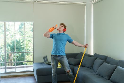 Handsome young man Caucasian people in casual wear, wearing headphones, carrying bottles of cleaning liquid, singing, and dancing music. Modern husband chores in fun and happiness as a house cleaner
