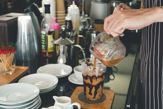 close-up photo of the hand is pouring freshly made cappuccino into a glass. barista Professional men making latte and espresso for customer service.  coffee shop owner is preparing drinks in the cafe.