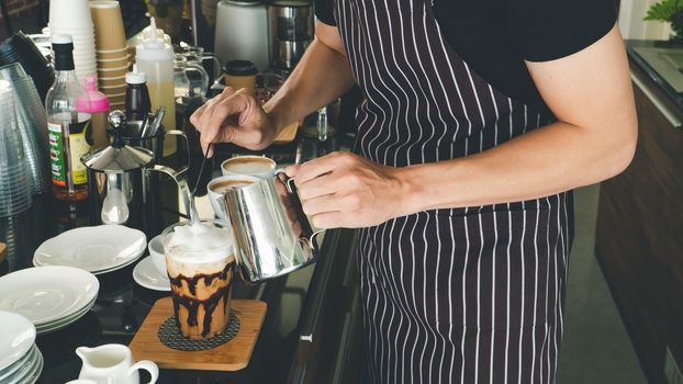 close-up photo of the hand is pouring freshly made cappuccino into a glass. barista Professional men making latte and espresso for customer service.  coffee shop owner is preparing drinks in the cafe.