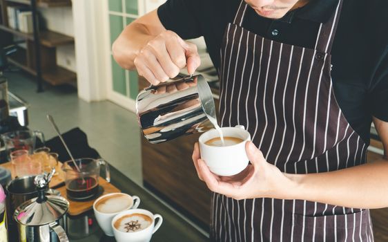 A close-up photo of hand pouring milk in a cappuccino glass. barista Professional men making latte and espresso for customer service. Coffee shop owners are preparing a drink in the cafe.