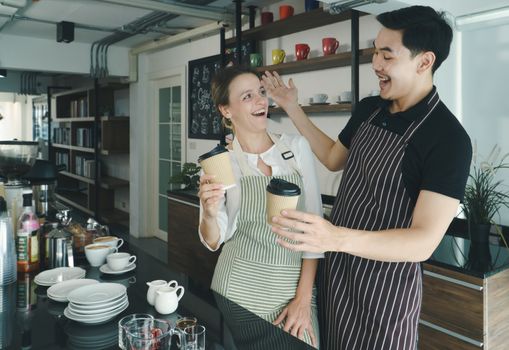 young Asian man talks with a Caucasian woman and laughed was happy. barista and waitresses discuss customer service in the coffee shop. The cafe work together, friendship, and relaxation concept.