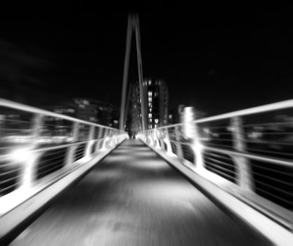 monochrome zoom blur image of a pedestrian footbridge in an urban setting at night with illuminated buildings and a dark sky