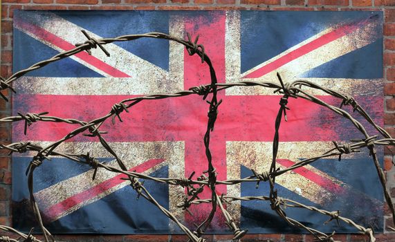 barbed wire in front of an old stained dirty union jack british flag with dark crumpled edges on a brick wall background brexit freedom of movement isolationist concept