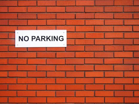 a white sign saying no parking on a red brick wall