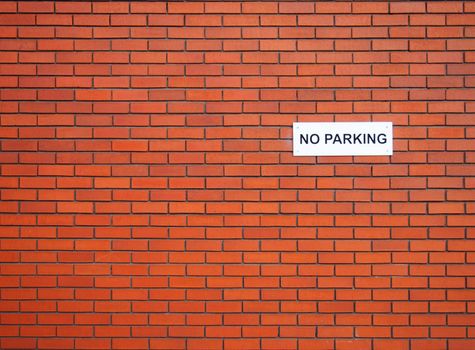 a white sign saying no parking on a red brick wall