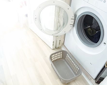 a washing machine with the door open and a small plastic basket to hold the freshly washed laundry. Interior of a house. Household chores and cleaning of clothes.