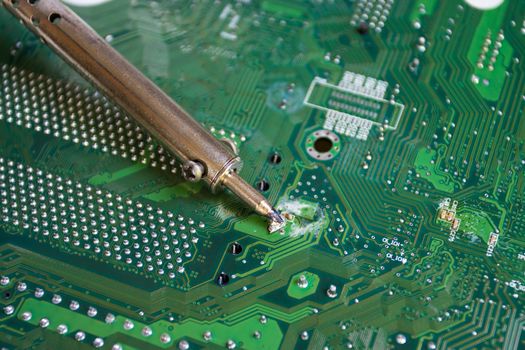 soldering iron on green mainboard for repairing electronic of the computer circuit board concept technology of computer circuit hardware
