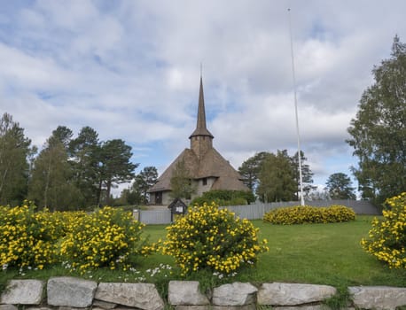 The old church of Dombas in traditional style with blooming yellow flowers. Blue sky, white cloud background. Oppland, Norway.