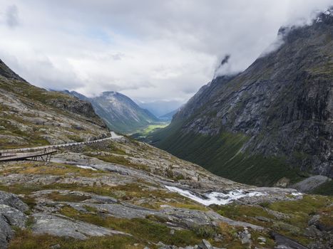 View point platform on Trollstigen or Trolls Path with green valley and waterfall at massif Trolltindene in Romsdal valley, Norway. Cloudy white sky clouds