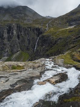 View point platform on Trollstigen or Trolls Path with green valley and waterfall at massif Trolltindene in Romsdal valley, Norway. Cloudy white sky clouds