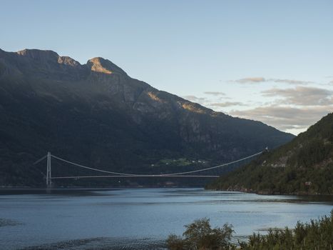 View on Hardanger Bridge across fjord Hardangerfjorden connects Ullensvang and Ulvikin, Norway. Longest tunnel to tunnel suspension bridge in the world 1380 meters. Summer day golden hour