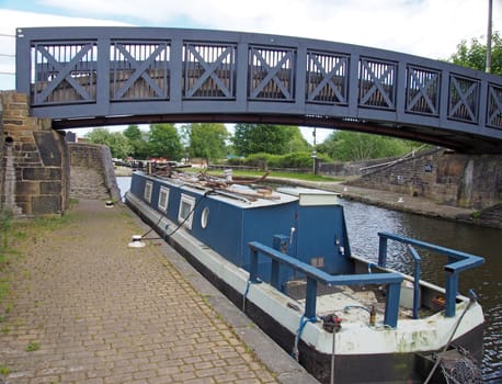 a blue footbridge crossing the calder and hebble navigation canal in brighouse west yorkshire with and old narrow boat moored underneath