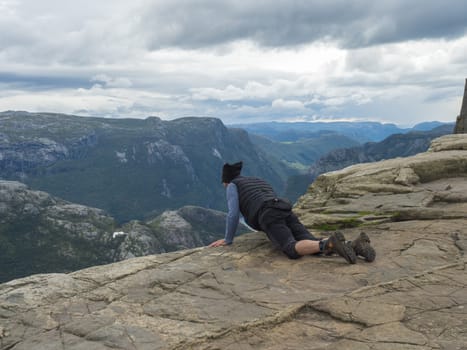 Lying men looking view on fjord Lysefjord over the Preikestolen cliff, famous Norway viewpoint. Moody autumn day. Nature and travel background, vacation and hiking holiday