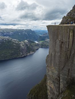 Profile view of famous Preikestolen massive cliff at fjord Lysefjord, famous Norway viewpoint with group of tourists and hikers. Moody autumn day. Nature and travel background, vacation and hiking holiday concept