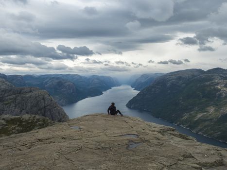 Hiker woman admiring view on fjord Lysefjord from Preikestolen massive cliff, famous Norway viewpoint. Moody autumn day. Nature and travel background, vacation and hiking holiday concept