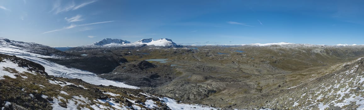 Wide Panoramic view from Krossbu on glacier Smorstabbreen, snow-capped mountains and blue lakes in Jotunheimen National Park, Western Norway.