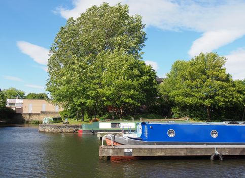 old narrow boats converted to houseboats moored in the marina at brighouse basin in west yorkshire surrounded by trees and a bright sunny blue sky