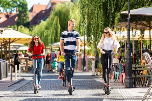 Trendy fashinable group of friends riding public rental electric scooters in urban city environment. New eco-friendly modern public city transport in Ljubljana, Slovenia.