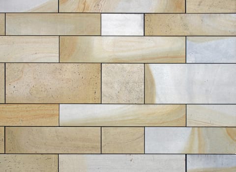 full frame image of a wall made of large flat blocks of textured yellow and grey york stone