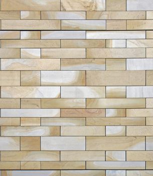 a full frame image of a wall made of large flat blocks of yellow and grey york stone with a marbled texture