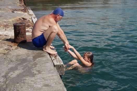 a man helps a girl to climb the pier from the sea