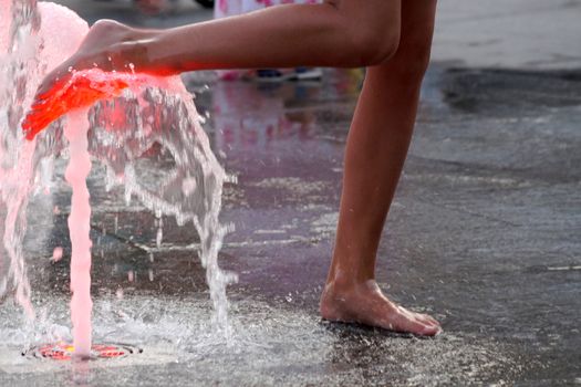 a girl touches a fountain on the sidewalk with her bare foot.