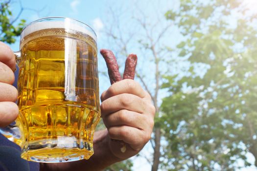 a mug with beer and sausages in the hands of a man close up