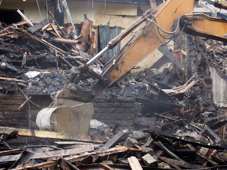 Hydraulic crusher excavator machinery working on a demolition site clearing burned debris with dust and smoke