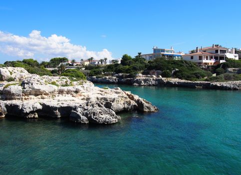 scenic view of the cala santandria in menorca with bright sunlit sea surrounded by cliffs and white houses overlooking the water