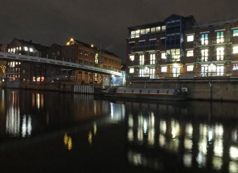 calls landing on the river aire in leeds at night with the lights of historic old buildings and apartments reflected in the water and a moored barge