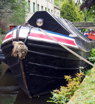 the bow of an old moored narrow boat on the rochdale canal in hebden bridge surrounded by grass trees and old buildings