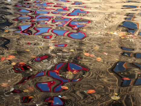 abstract image of red windows of an old stone building reflected in the ripples of dark water with floating autumn leaves