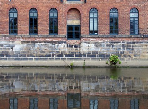 an old brick canal warehouse in leeds with windows reflected in the water