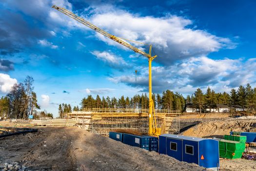 Photo of new bridge building site with timbering construction for further filling it with concrete. Yellow crane tower, blue clouds, deep ditch. A lot of building materials - steel and wooden parts