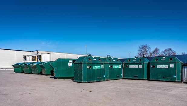 Large public recycling station at parking lot for disposal of different household waste - plastic, metal, paper, carboards. Northern Sweden, Umea. Sunny day. Green metal containers sorted recycling