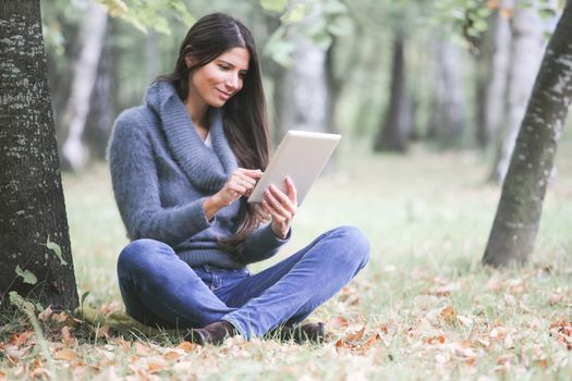 Smiling young woman using digital tablet sitting in autumn park