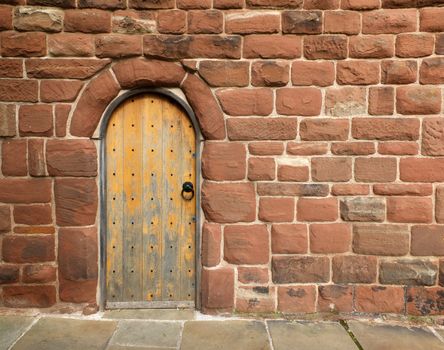 an ancient brown wooden door in a red sandstone medieval wall