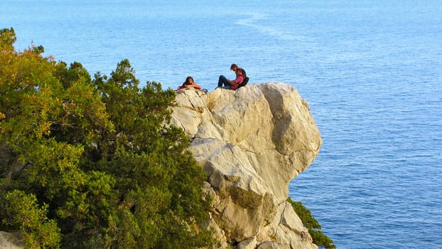 Two men and a woman resting on a ledge of rock above the sea                               