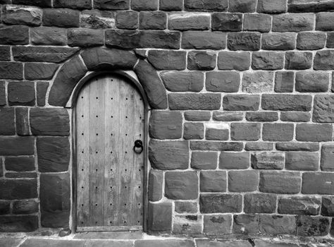 a monochrome image of an ancient wooden door in a stone medieval wall