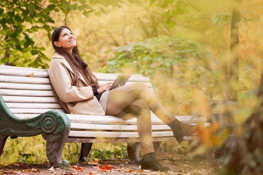 Smiling young woman using digital tablet sitting in autumn park