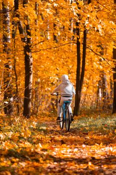 Boy riding bicycle in autumn orange maple tree park on a dirt road in the woods