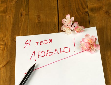 White sheet of paper with the inscription "I love you" on a wooden surface lies